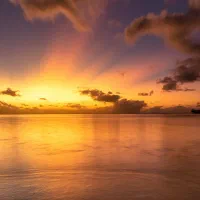 Sunset over a calm shoreline, with rocks in the foreground