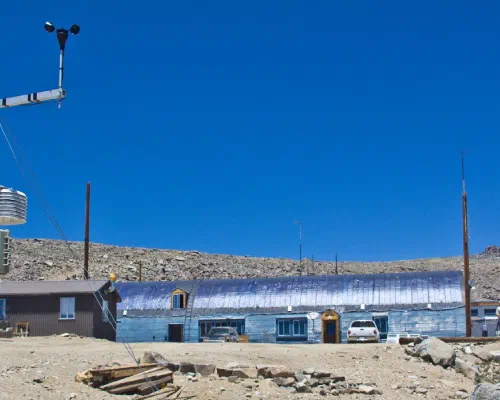Weather monitoring equipment stands near a small research station in a barren, rocky landscape
