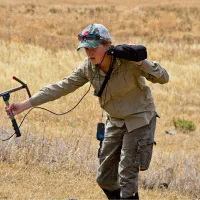 A researcher walking through a dry grass field with tracking equipment